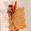 Bouquet of dried flowers with a wooden plaque and handwritten message on a neutral background